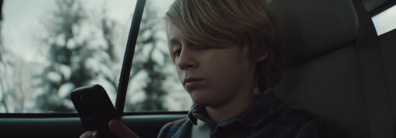 A boy is looking at his phone in the car
