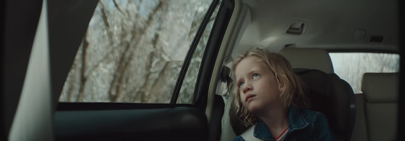 Girl sitting inside a moving car looking out the window at the passing trees