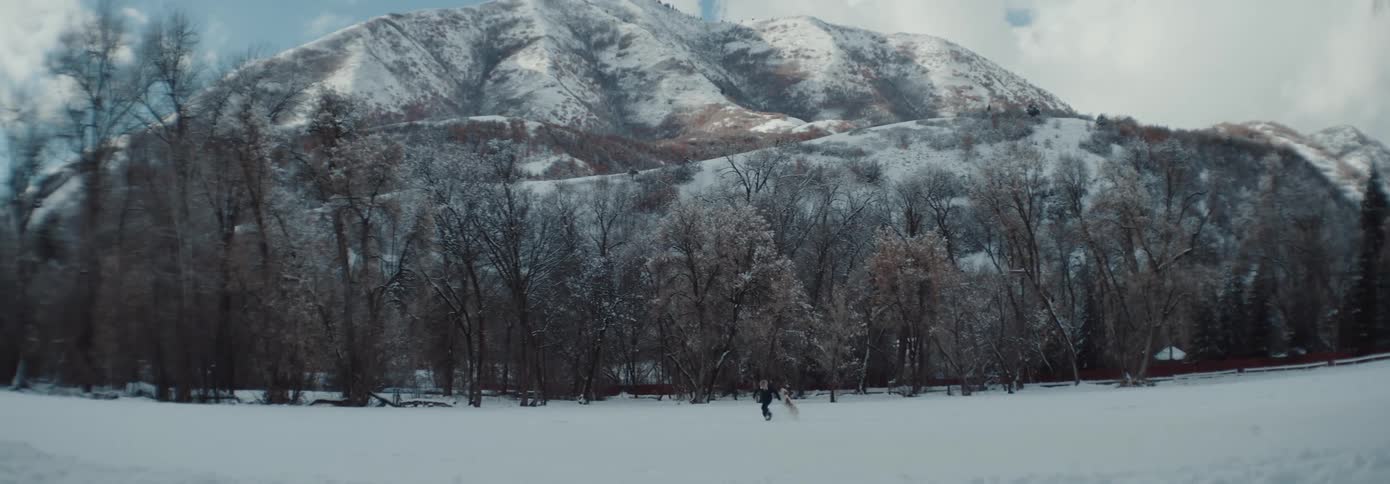 Boy and dog run through snow with mountain in the background