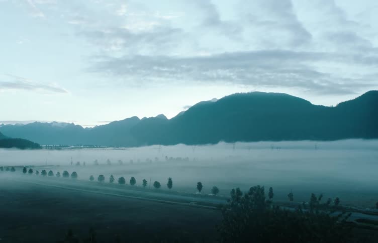 Lake surrounded by trees with a mountain range in the distance under a cloudy sky