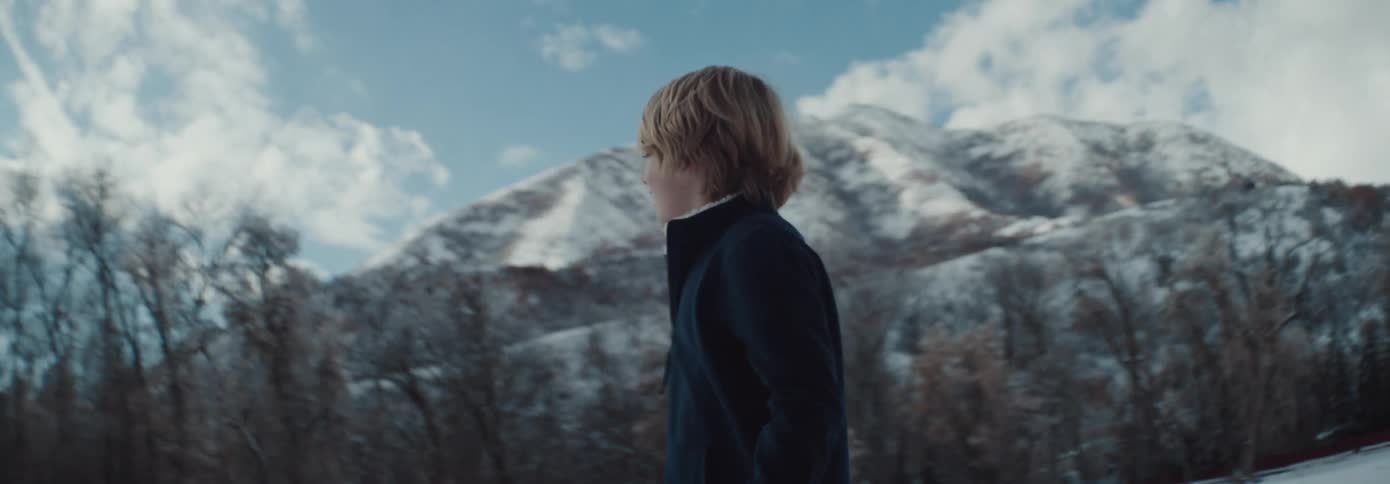 A boy is walking in the snow by the mountain