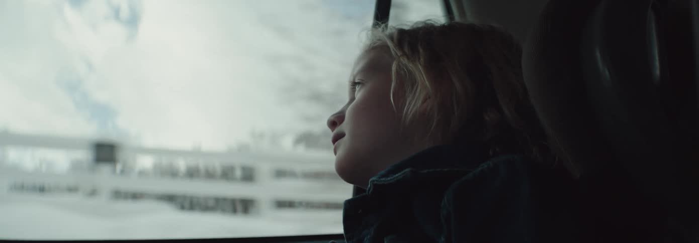Blonde girl sitting in the back of a car looks out the car window