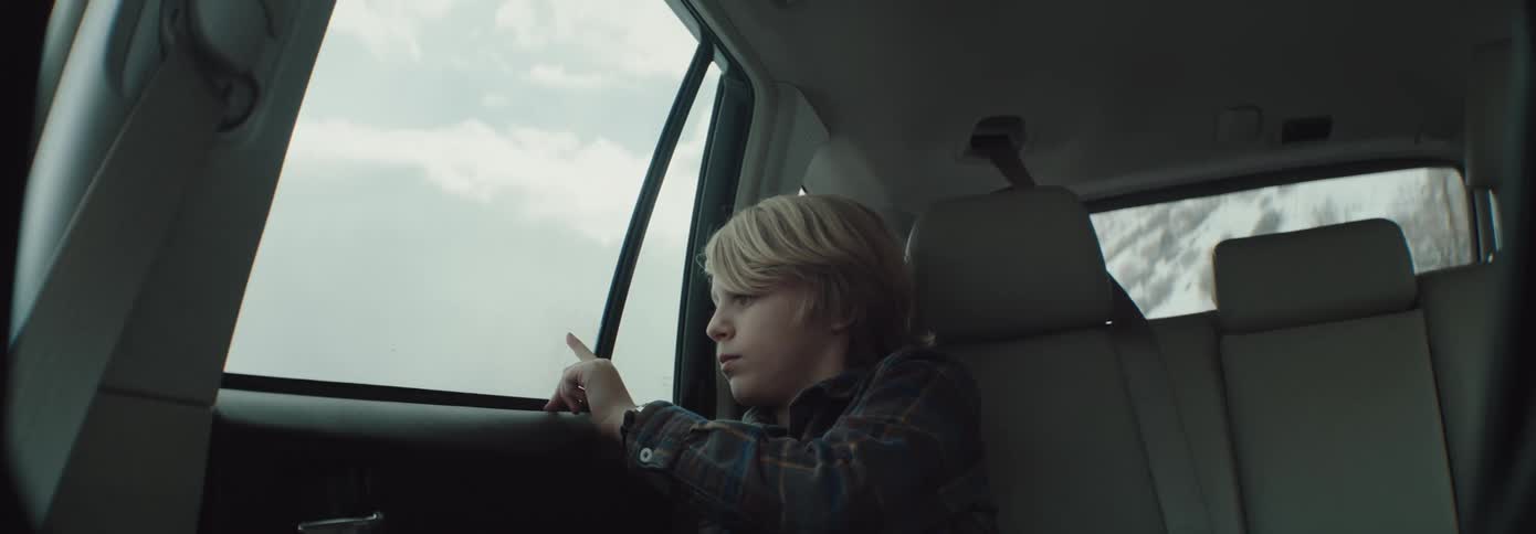 Blonde boy sitting in the back of a car touches car window