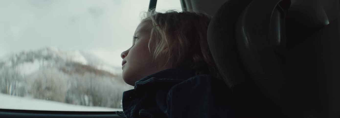 A girl looks out the window of a car at snow covered trees and ground