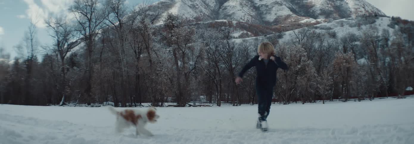 A boy and dog run together outside in the mountain snow