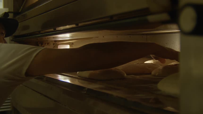 Baker organizing loafs of bread inside an oven in a bakery