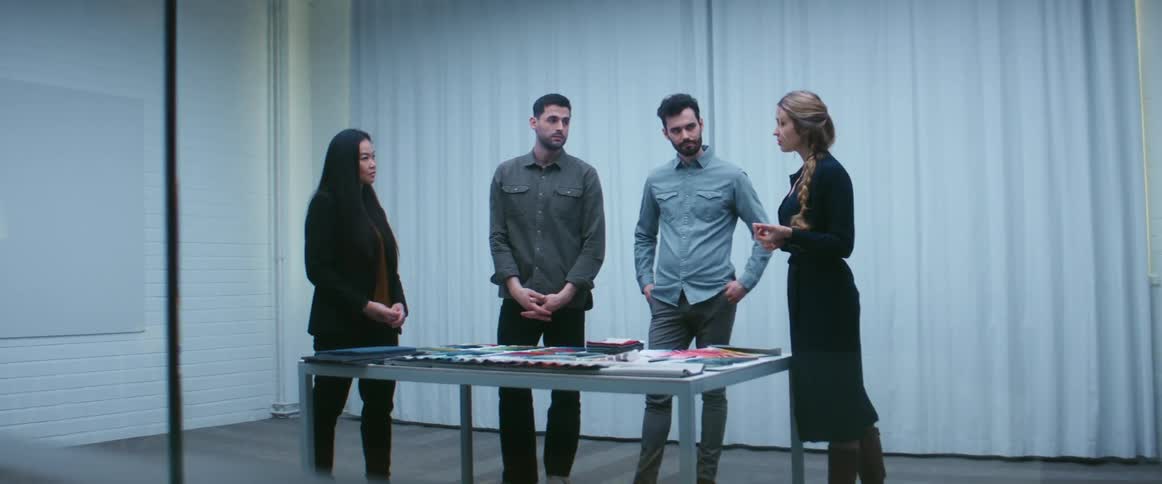 Two men and two women standing around a table and talking with a curtain and a wall in the background