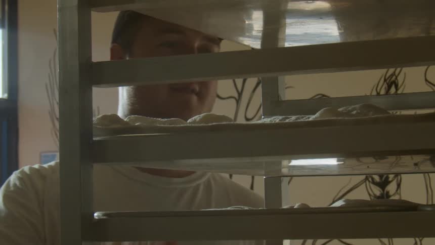 A man sliding a tray of bread dough onto a rack in a bakery