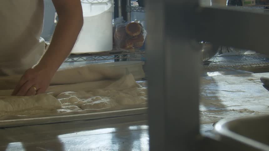 A man preparing dough on a pan in a factory bakery setting