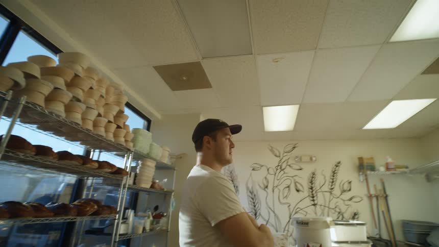 Man walks into kitchen of bakery and stands looking around as pedestrian walks past store door