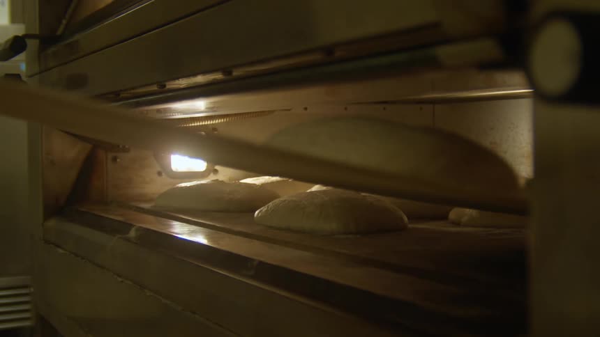 Baker organizing loafs of bread inside an oven in a bakery