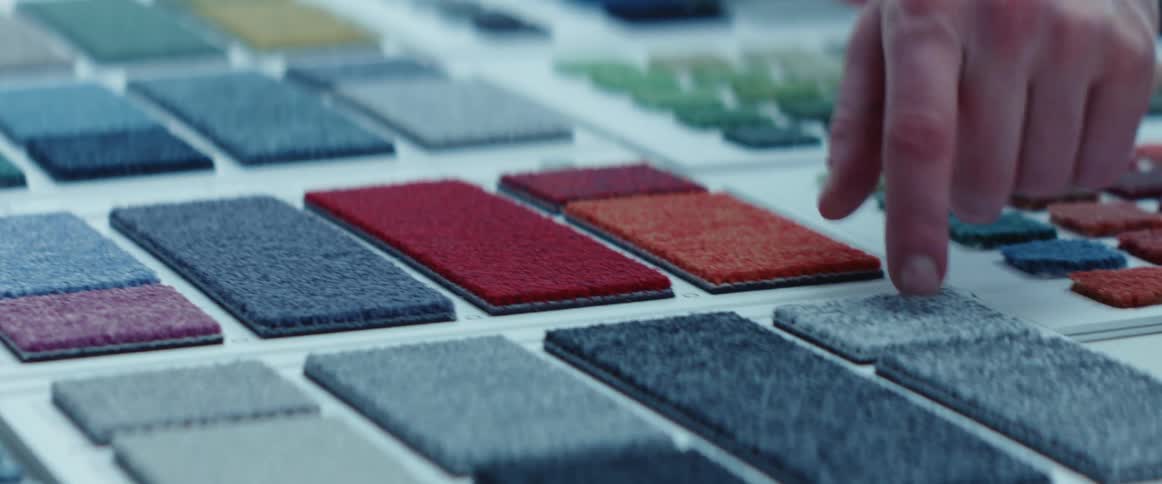 A man chooses carpet samples from a display table of options against a white background