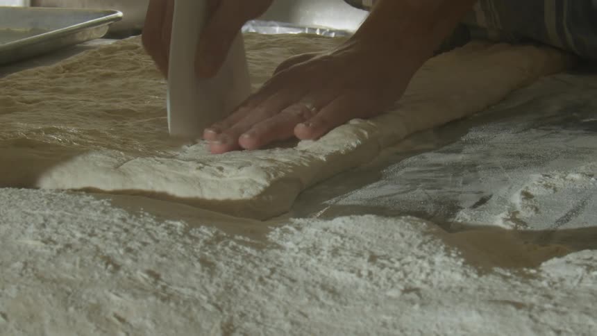 A person cutting loafs of bread from fresh dough