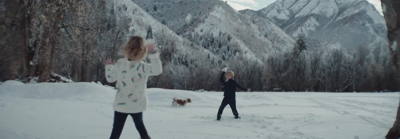 Boy and girl throw snowball at each other in the snowy field with snowy mountains in the background