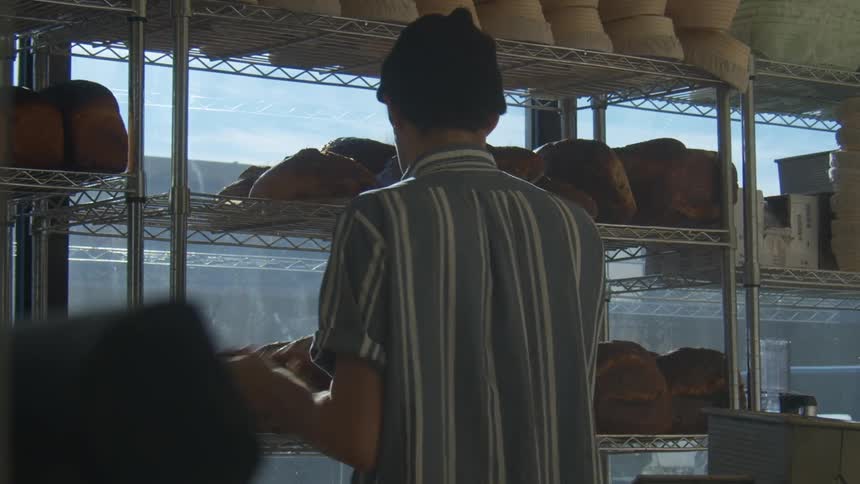 A baker organizing freshly made bread on the shelfs of a shop