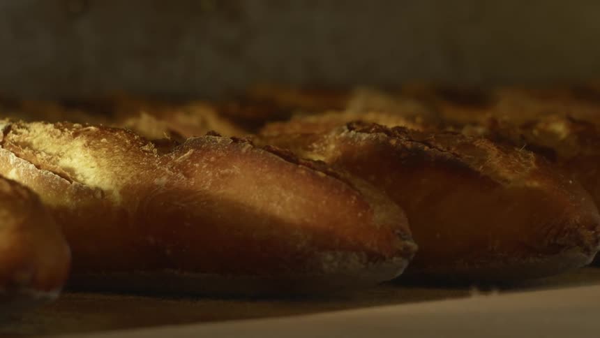 A baker removes loaves of bread from a large oven