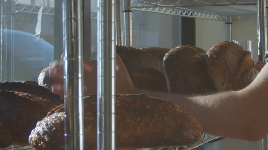 A person in a bakery adjusting bread on a shelf next to a glass window
