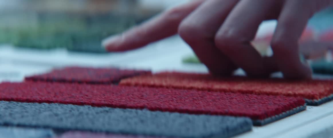 A woman touches and taps on a fabric sample laid out on a table with others