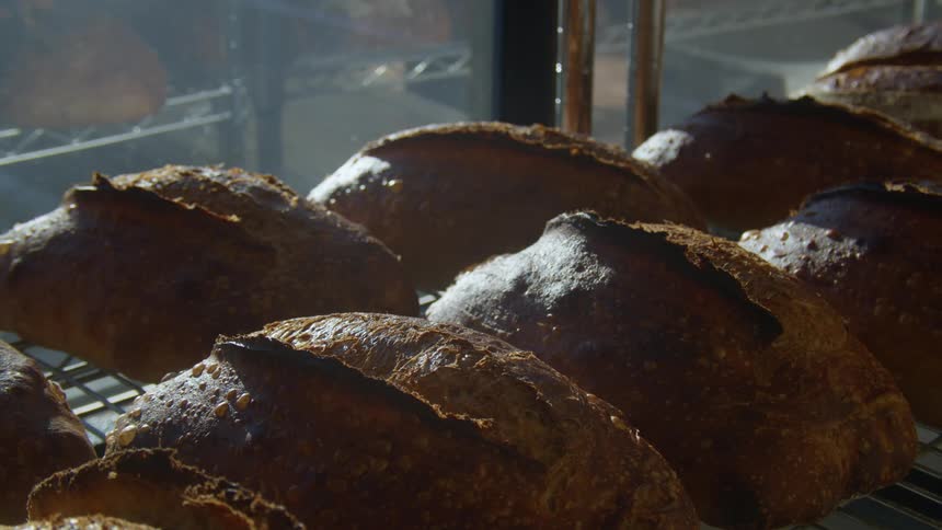 Rows of baked bread sitting on a wire shelf in a bakery