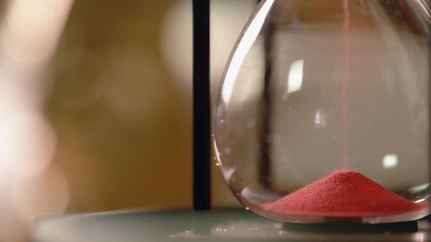 Red sand flows and piles in an hourglass
