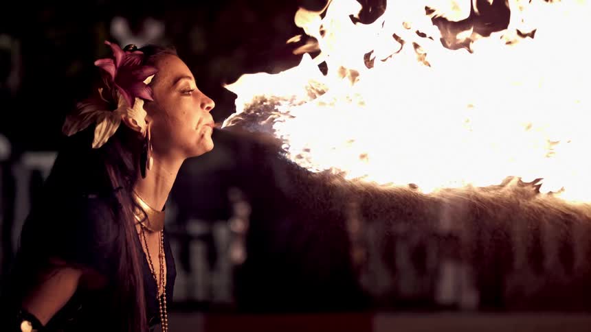 A woman spewing flames using her mouth outdoors