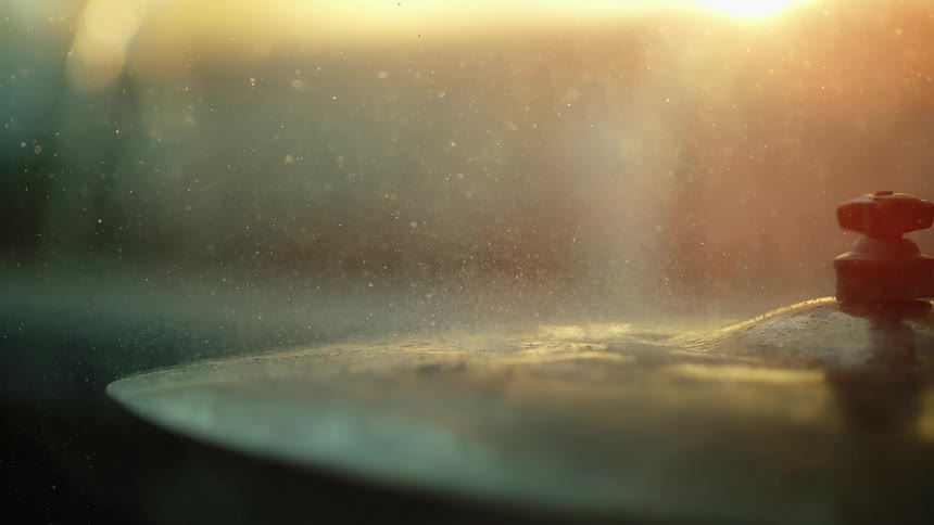 Sun shines onto cymbal hit by drum stick spreading water droplets into the air