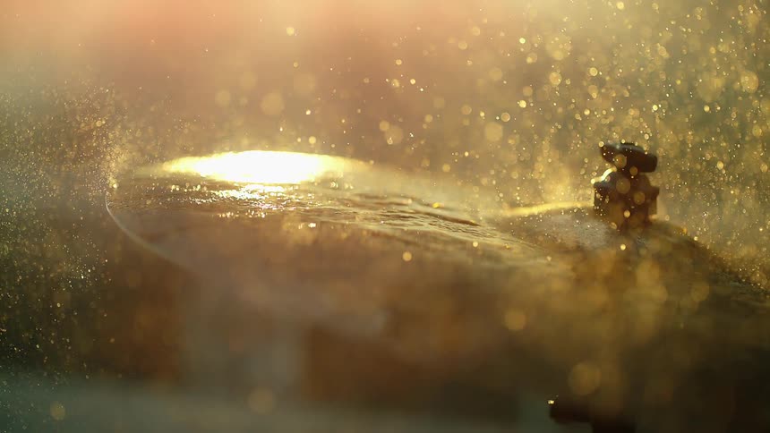 A drum stick strikes a wet cymbal causing droplets of water to fly up and sparkle in sunlight