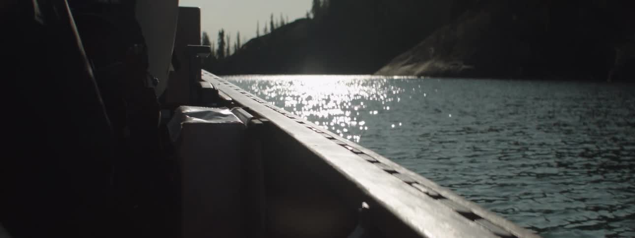 A small boat sails down a river past barren trees on the shoreline