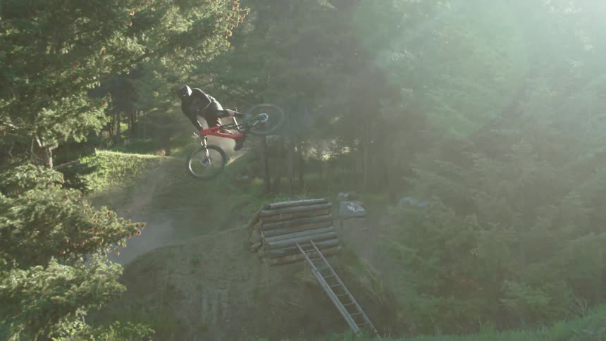 A mountain bike athlete whips sideways after hitting big jump in a forest during the morning light