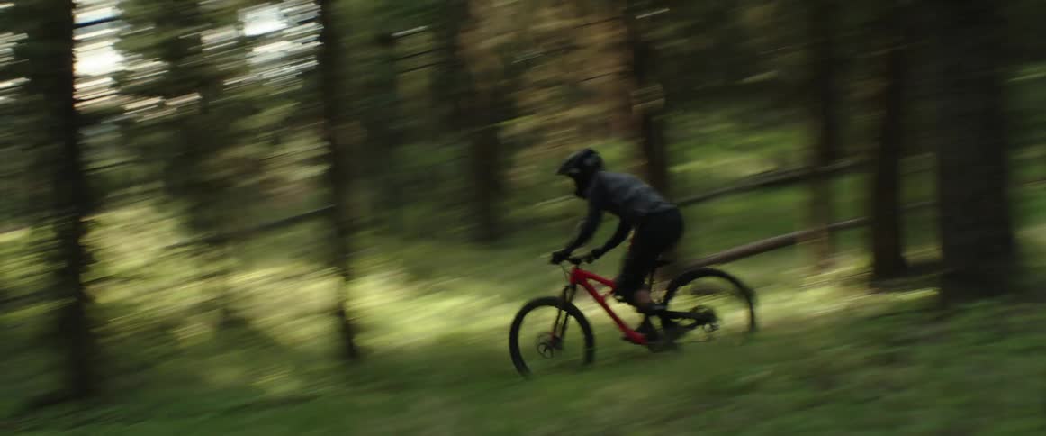 Cyclists rides bike through green meadow on fast downhill dirt trail