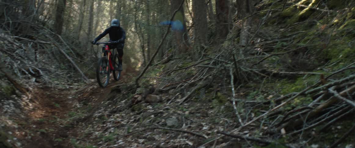 Bicyclist rides mountain bike down forest trail and hits corner kicking up dirt