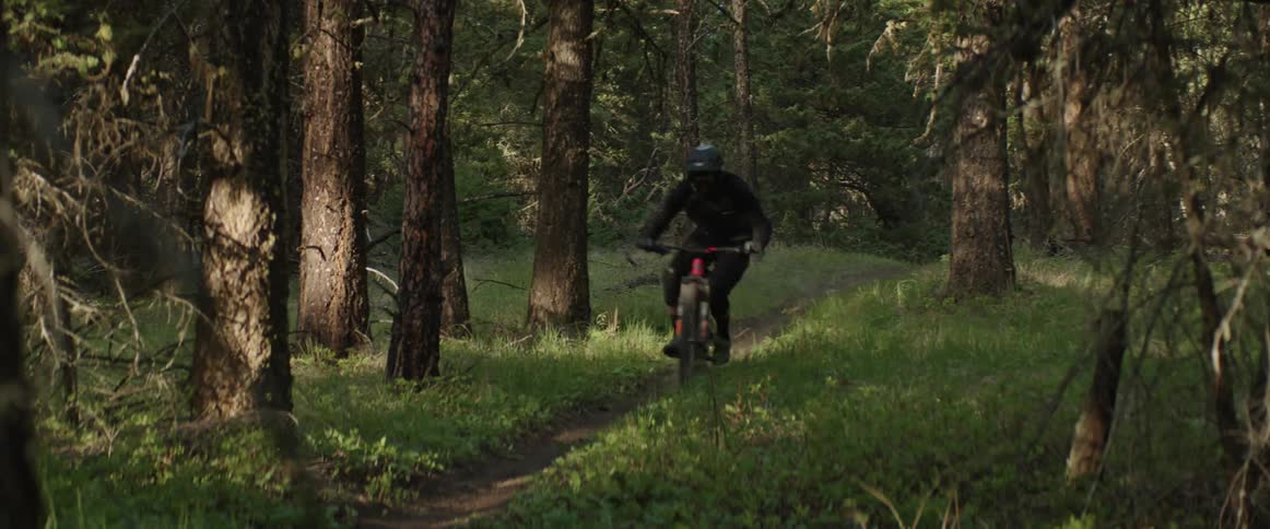 A mountain bike athlete rides bicycle down dirt trail in a green meadow