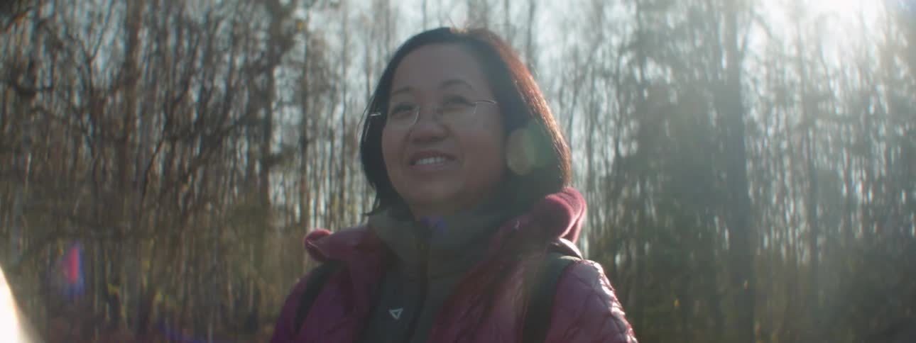 A woman standing in a forest smiles