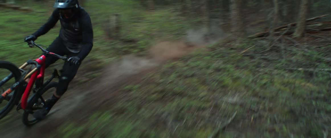 Cyclists rides bicycle down dirt trail cutting through forest on slope