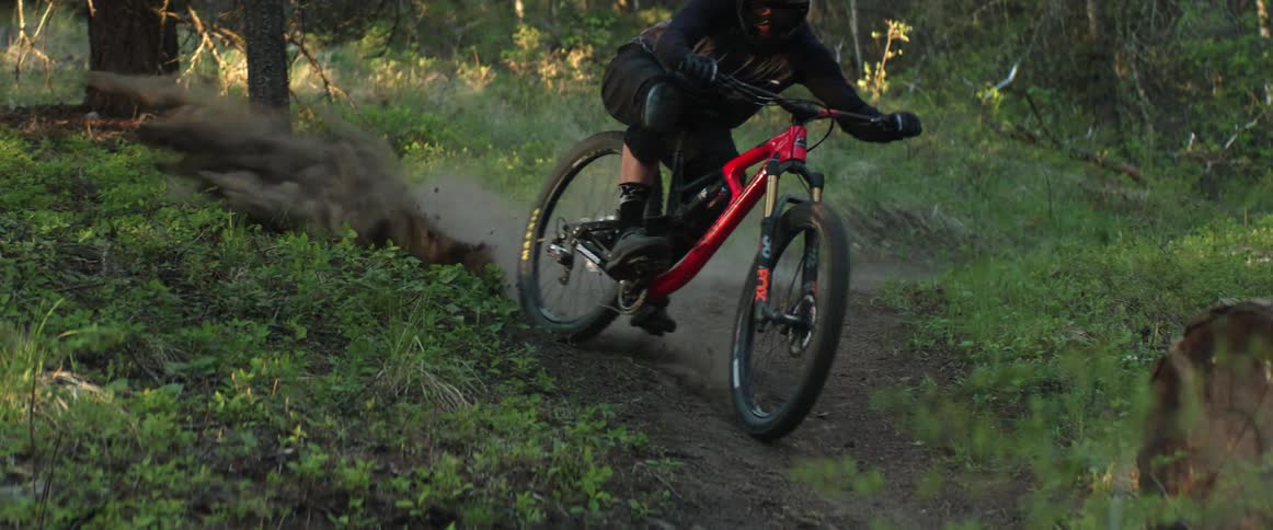 A mountain cyclist kicks up dust and dirt as he comes around a corner on green forest trail