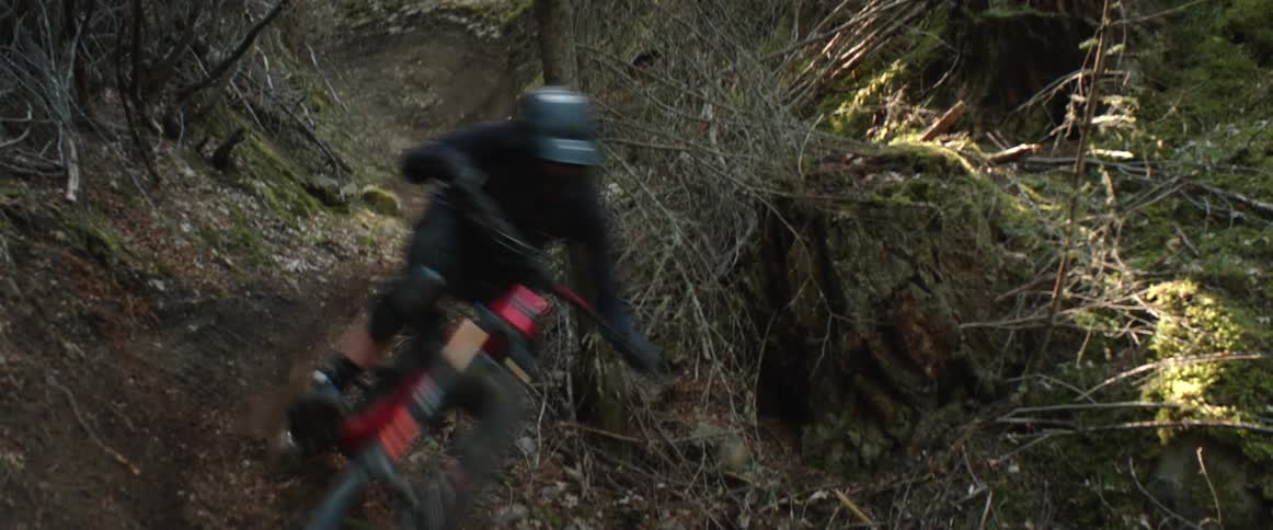 A person riding a bicycle through fast dirt corners in a forest ravine trail