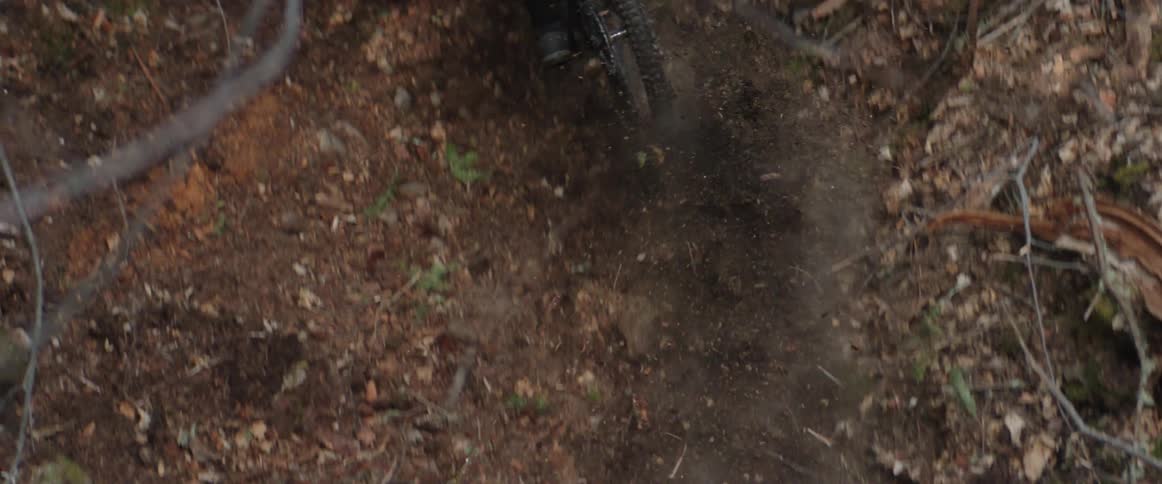 A person with a helmet riding a bike in a forest kicks up trail of dirt behind tire