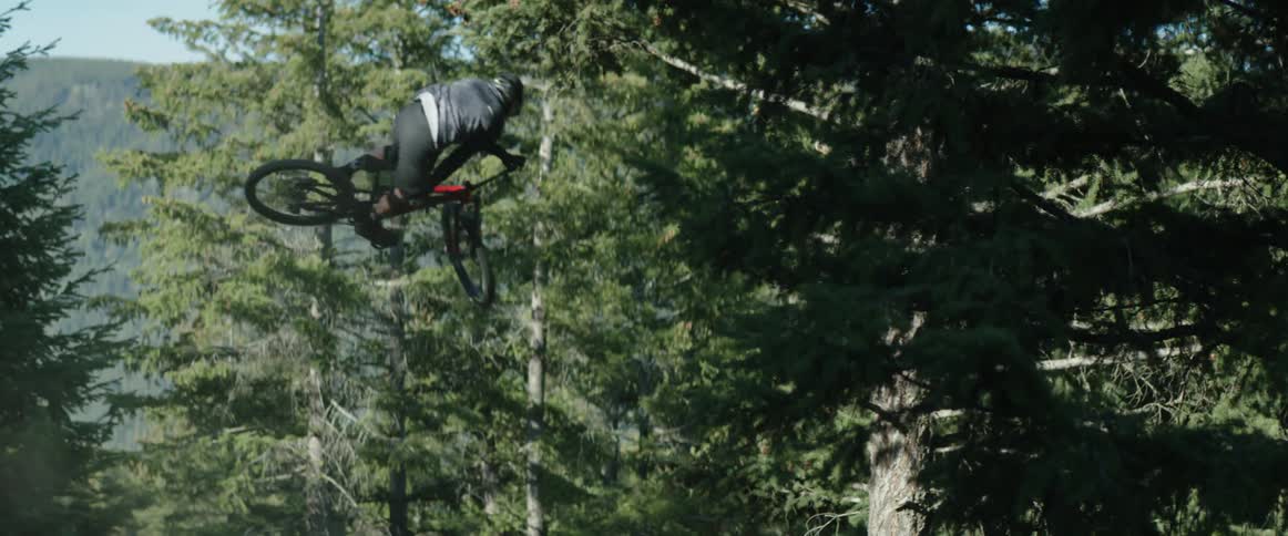 A man mountain bikes in a forest and whips his bike sideways