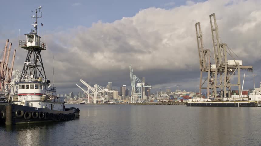Reveal of downtown Seattle from behind container cranes and tug boats along Harbor Island
