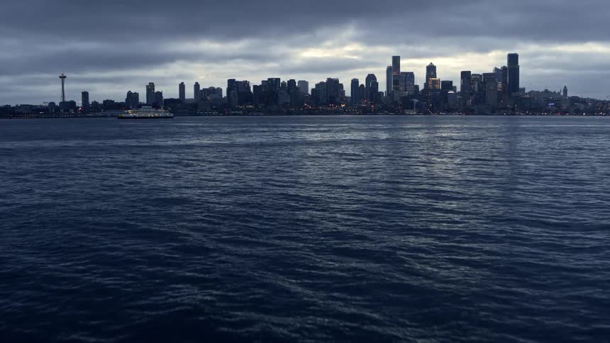 Skimming over Elliott Bay to reveal the Seattle skyline at sunrise under cloudy skies