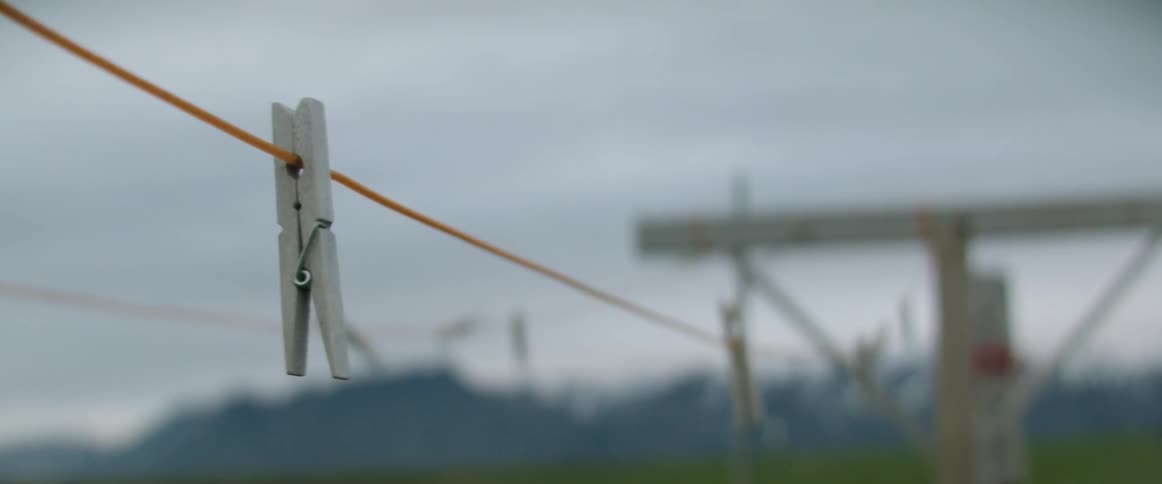 Clothespins on a clothing line with a grassy field the sky and clouds in the background