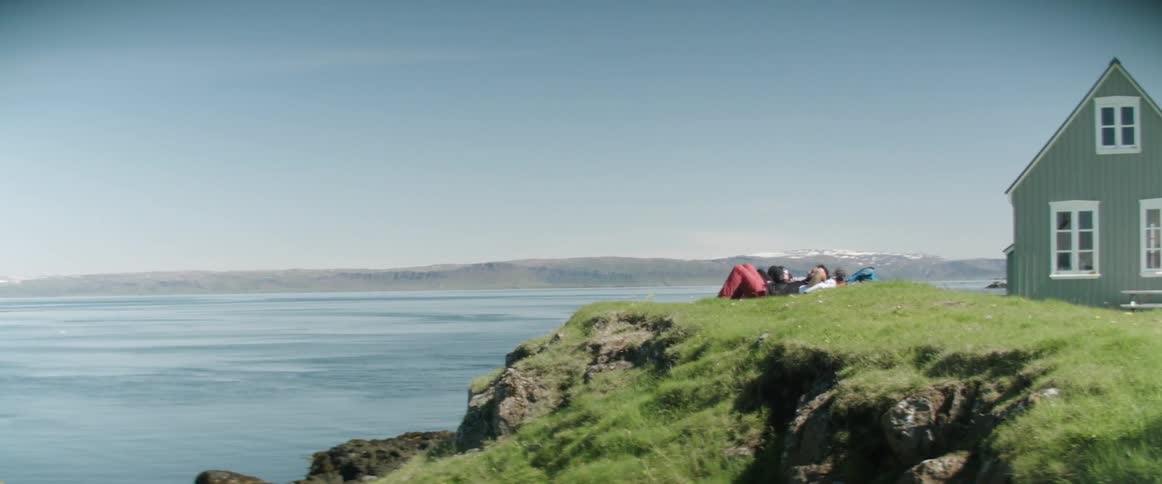 Three men lie on their backs outside a home on a cliff overlooking the ocean