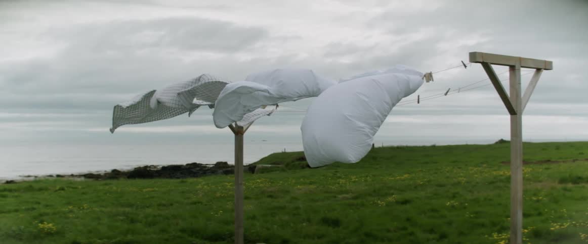 Clothing blowing in the wind on a clothing line on a grassy field with the sky and clouds in the background