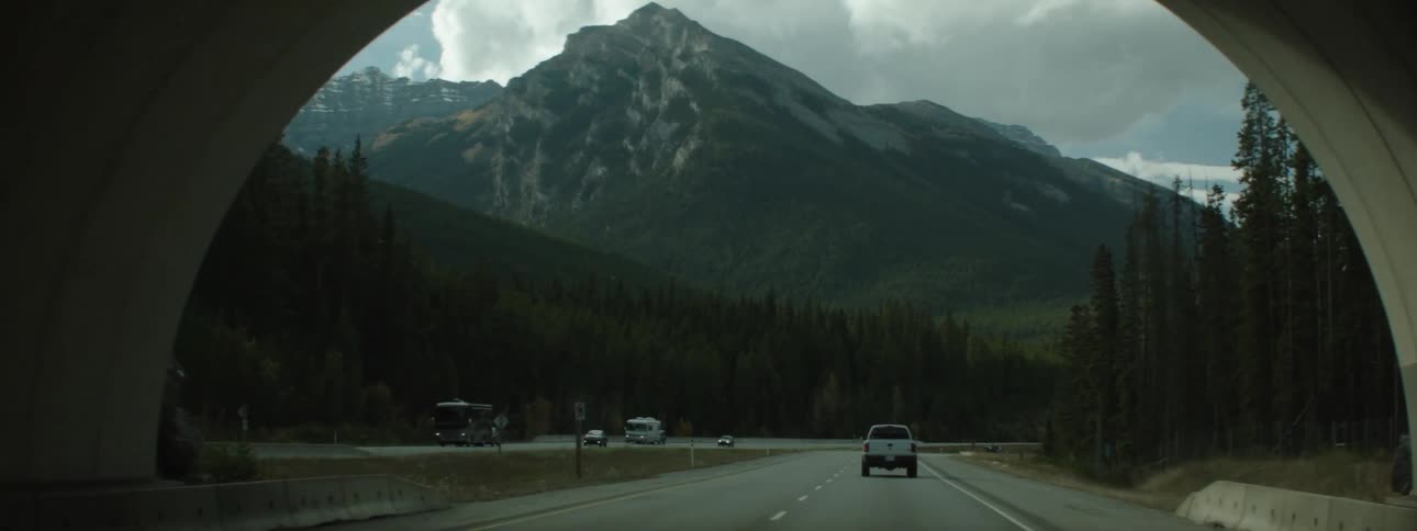 Vehicles drive through a tunnel on a highway with views of a tall mountain