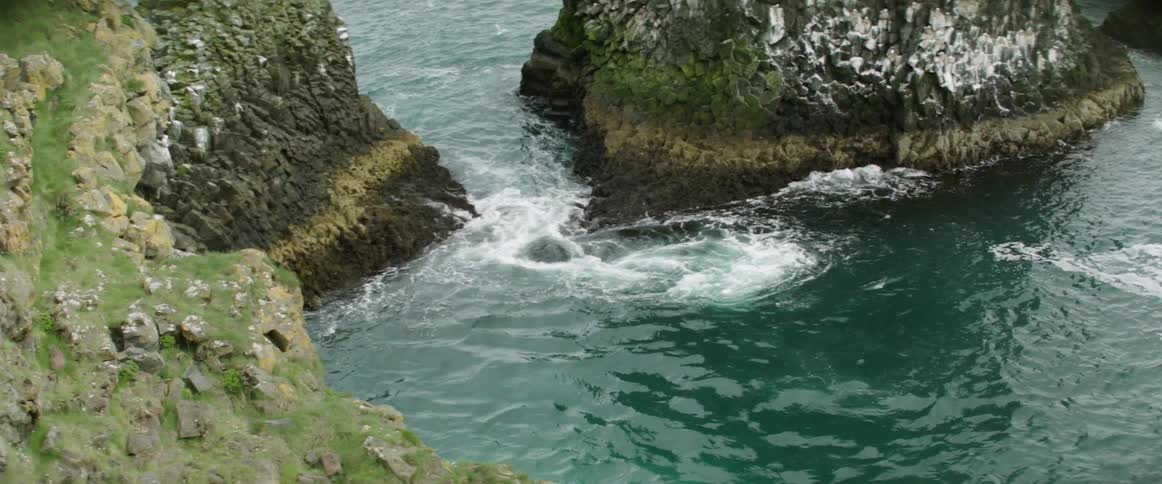 Birds fly over swirling water near inlet between steep sloping shores