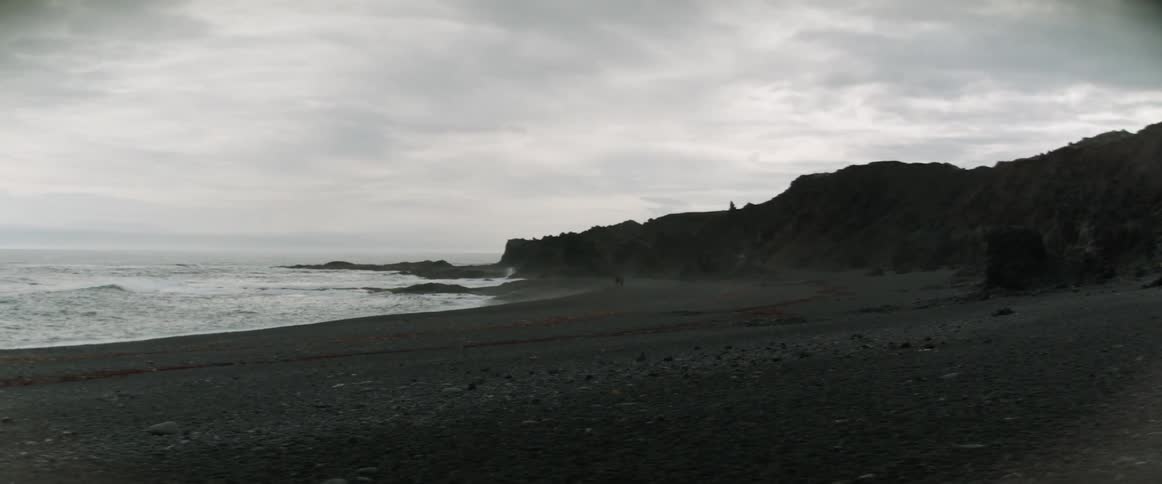 Two people walk along the shore of a rocky beach