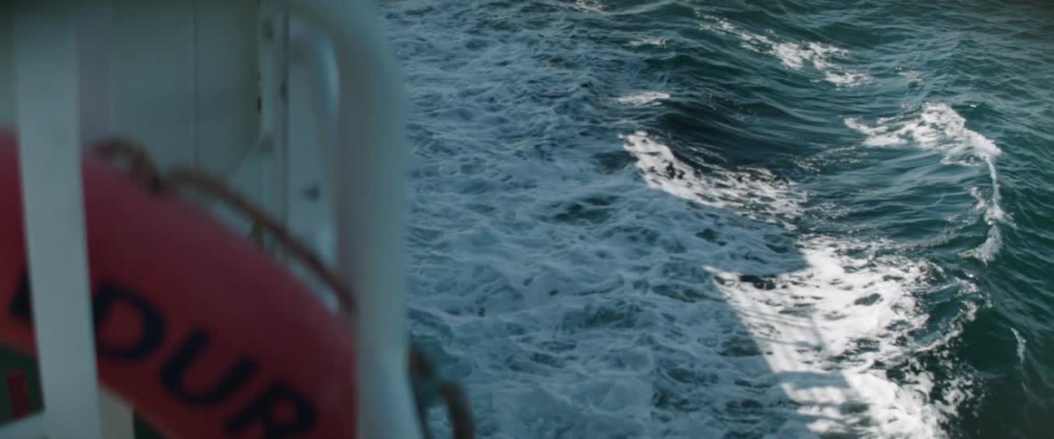 A life preserver sits tucked behind a handrail on a boat as it sails through the ocean