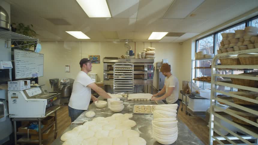 Three men in a bakery shaping dough on a table with flour