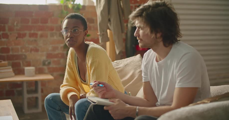 A woman talks with a man while they sit together on a sofa in house during the day