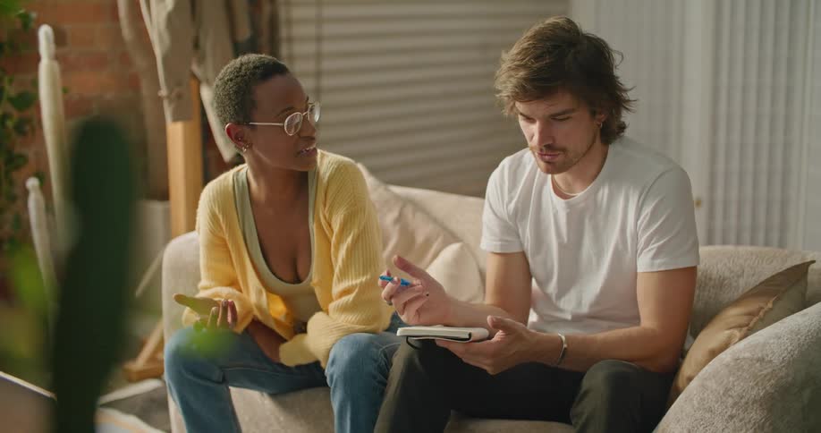 A man and woman sit on a couch together while reviewing information on a laptop